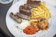 A plate with cevapcici, fries, rice and raw onions