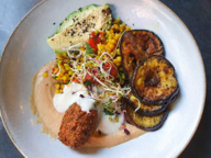 A plate of fried aubergine, corn, avocado and other vegetarian food.