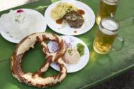 Vista di un tavolo verde in un giardino della birra a Monaco con due bicchieri di birra, pretzel, obazden e ravanelli.