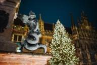 A statue in front of the town hall and an illuminated Christmas tree at the Christkindlmarkt on Marienplatz in Munich