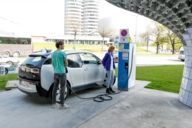A man and a woman are standing with an electric car in front of a charging station at BMW Welt in Munich.