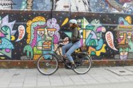 Woman on a bicycle in front of a wall with graffiti in Munich.