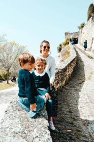 Carina and her children sit on a stone wall in the sunshine.