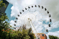 A Ferris wheel against a cloudy sky. Skyscrapers can be seen in the background.