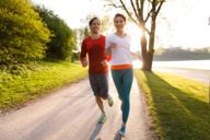 A woman and a man are jogging through the Olympic Park in Munich in the evening sun.