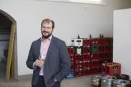 A man stands with a beer glass in his hand in front of many beer crates and kegs.