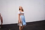 A woman who is wearing a dirndl is standing in front of a building at the Oktoberfest in Munich.