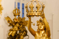 Golden figure holding up crown in both hands.