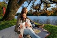 A couple is sitting on a picnic blanket at Nymphenburg Schlosspark in Munich on a sunny day in autumn.