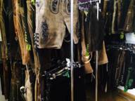 Many different leather pants hang on clothing racks in a store.