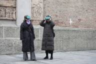 Two women in winter coats stand in front of Munich's Frauenkirche wearing VR glasses