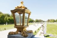 In the middle is a golden lantern and in the background the park of Nymphenburg Palace in Munich.