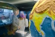 Un hombre señala con el dedo el globo terráqueo de la vitrina del Museum Mensch und Natur de Múnich y se lo muestra a su hijo, al que lleva en brazos.