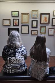 Two seated women look at a wall of paintings.