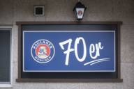 A house wall with a blue sign saying "70er" and the "Paulaner" sign in Munich.