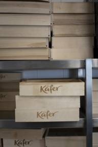 Wooden boxes with the Käfer logo are stacked on a shelf.