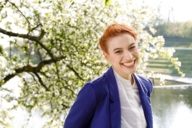 A woman is standing in front of a blossoming tree in the Olympic Park in Munich and is smiling.