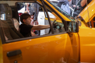 A boy sits at the wheel of a yellow car.