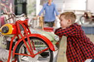 Child with plaid shirt looks at a historic motorcycle up close at the transportation center.