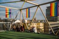 Several people sit on a roof terrace in Munich and rainbow flags hang on the building.