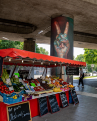 A hand painted on a concrete pillar raised to the Victory sign. In the foreground a fruit and vegetable stand.