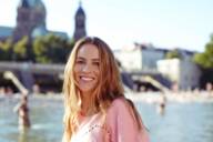 A young woman is standing in front of the Isar River in Munich on a sunny day.