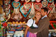 Two people are standing in front of a gingerbread heart stand at the Wiesn.