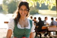 A woman is wearing a dirndl and is smiling in a beer garden in Munich by evening sun.