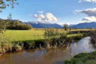 A view of the Murnauer Moos in the south of Murnau in sunny weather with a stream and mountains in the background