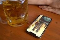 A smartphone lies on a beer table next to a pint of beer