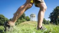 In the background the Monopteros in Munich, in the foreground the legs of a person walking through the English Garden.