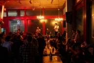 A band of three men plays music in a cosy bar in front of an audience.