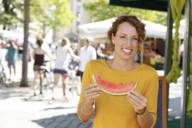 A woman in a yellow jumper eats a melon at the Viktualienmarkt.