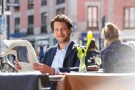 A man is reading a newspaper in a street cafe at Gärtnerplatz in Munich.