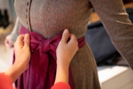 In the traditional dress store Gottseidank in Munich, a woman is tying the apron of another woman who is wearing a dirndl.
