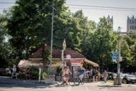 A man who is wearing swimming trunks is standing in front of the Reichenbachkiosk in Munich.