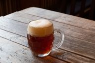 A dark beer in a bulbous glass on a wooden table.