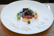 A white plate with a meat dish stands on a wooden table in the Michelin-starred Mountain Hub Gourmet in Munich.