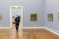 A man with glasses and beard is going through the Neue Pinakothek in Munich and is looking at the paintings.