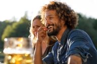 Un uomo con i capelli ricci è seduto in una birreria all'aperto a Monaco e sta sorridendo.