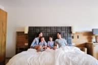 Carina and Jose are sitting in a hotel bed with their children.