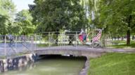 A woman in a dirndl drives her rickshaw over a small bridge in the English Garden.