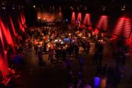 In the red-lit Muffathalle, many people stand in front of the stage