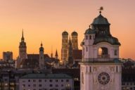 Panoramic view of the inner city of Munich at sunset with the Müllersches Volksbad in front and the towers of the Alter Peter, Heilig-Geist-Kirche and Frauenkirche in the background.