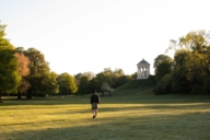 A man in lederhosen walks alone across a wide meadow in Munich.