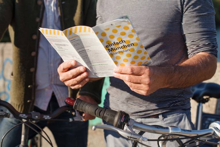 A man is holding a city map of Munich in his hands. A bike is besides him.