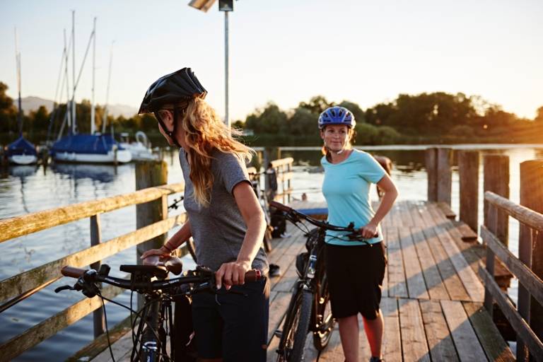 Two women with a bicycle on a pier by a lake in Bavaria.