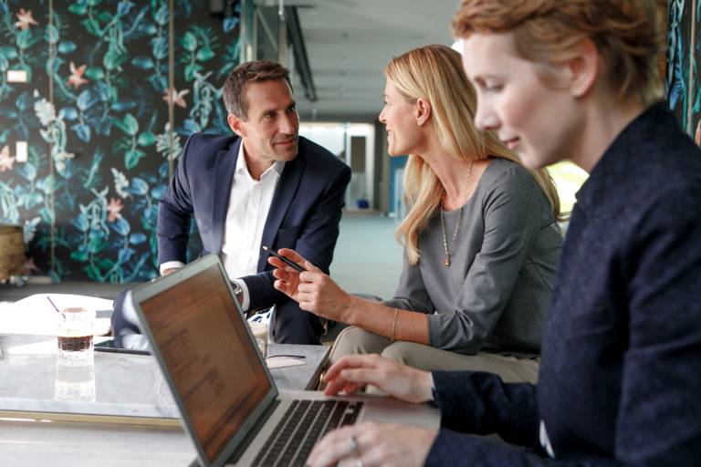 Two women and a man working at at table with a laptop in a hotel in Munich.