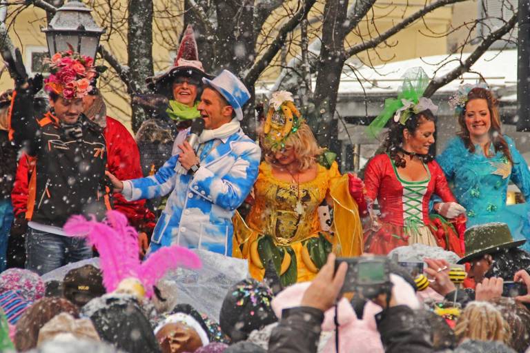 People in carnival costumes on an outdoor stage in driving snow.