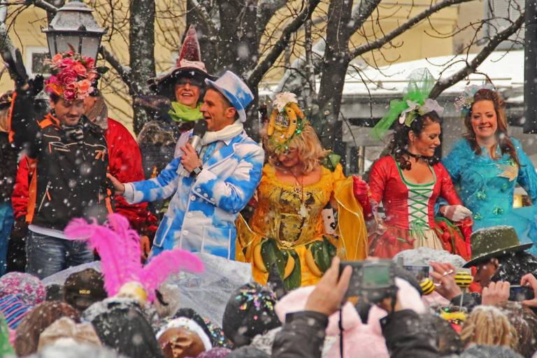 People in carnival costumes on an outdoor stage in driving snow.